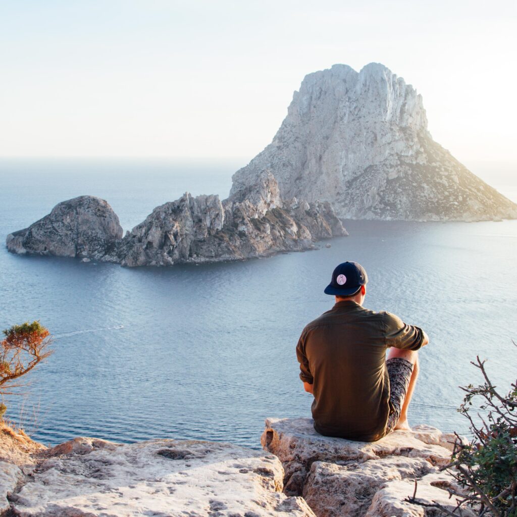 Hombre sentado en un acantilado con vistas al mar